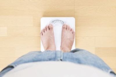 Mensch steht mit nackten Füßen auf Waage wegen Bluthochdruck durch Übergewicht